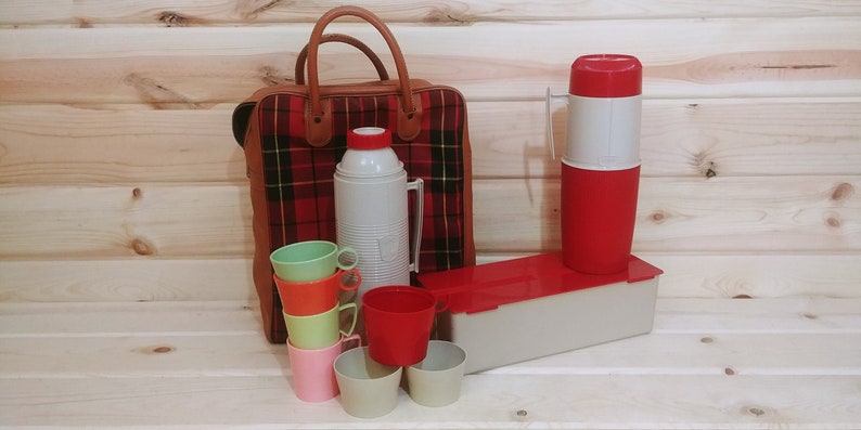May include: A vintage picnic set with a plaid bag, two thermoses, and six plastic cups in various colors. The thermoses are red and white, and the cups are green, orange, yellow, pink, and beige.