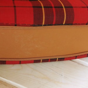 May include: The bottom of a red and black plaid bag with a brown leather bottom and gold metal accents.