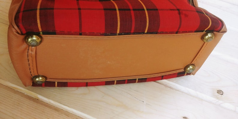 May include: The bottom of a red and black plaid bag with a brown leather bottom and gold metal accents.