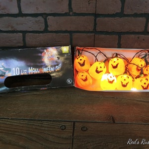 May include: A box of 10 light Halloween string lights with orange pumpkin-shaped lights. The lights are lit and the box says "10 Lite Halloween Set".