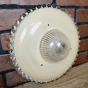 May include: A white ceiling light fixture with a beaded edge and a textured glass dome in the center.