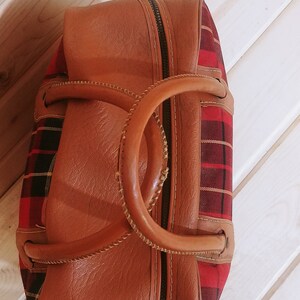 May include: A brown leather and red plaid travel bag with a top handle and zipper closure.