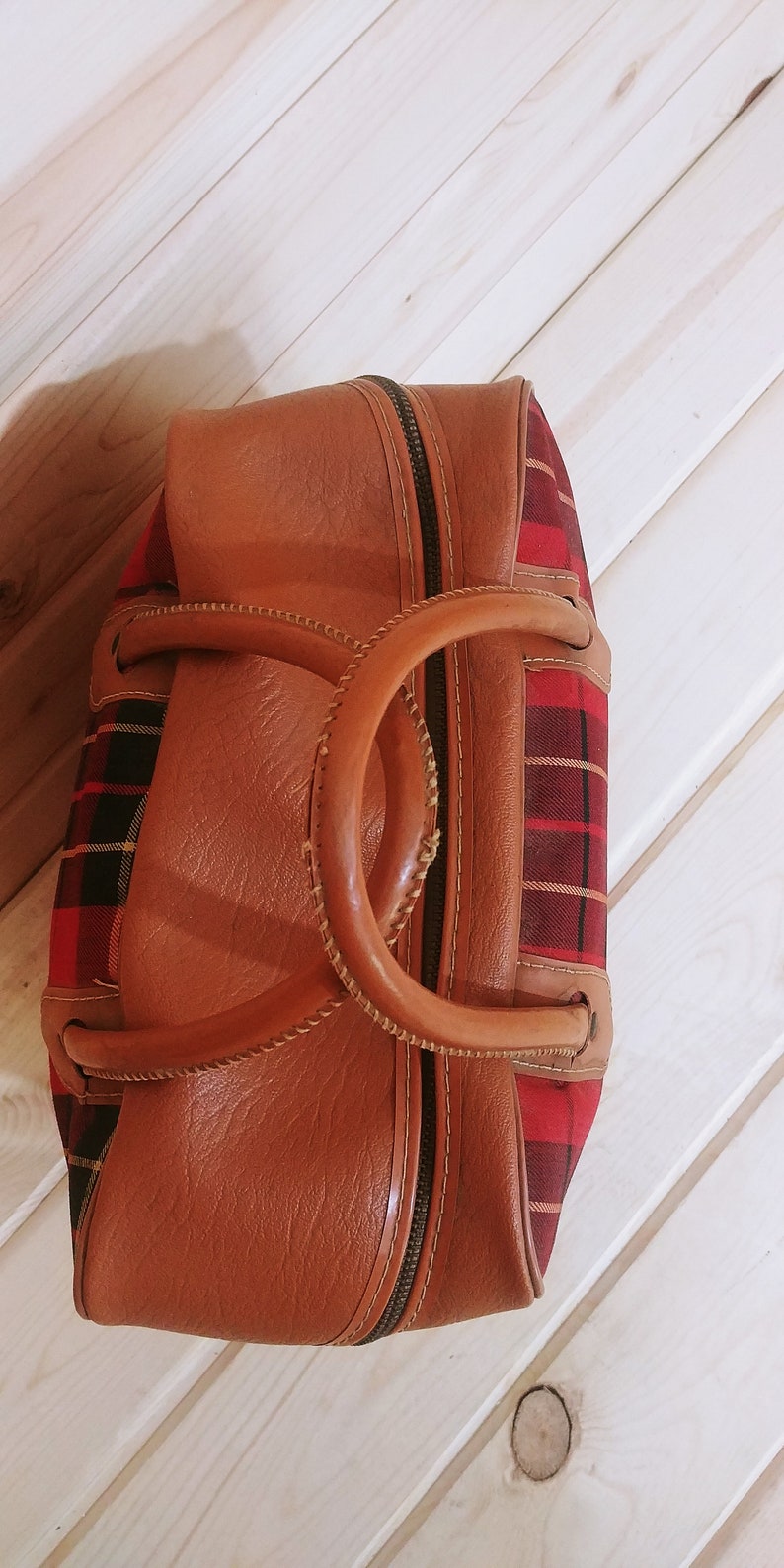 May include: A brown leather and red plaid travel bag with a top handle and zipper closure.