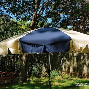 May include: A large, yellow and blue patio umbrella with a black trim. The umbrella is open and is in a backyard setting.