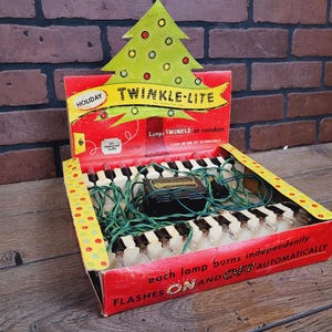 May include: A box of Christmas lights with a green tree and the words "Twinkle-Lite" on the front. The box says "Holiday" and "Each lamp burns independently, flashes on and off automatically".