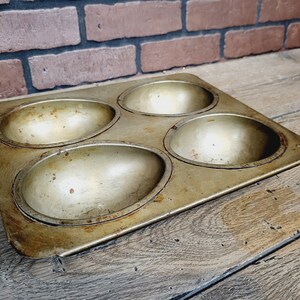 May include: A vintage metal baking pan with four round, slightly indented cavities. The pan is worn and has a slightly rusty patina.