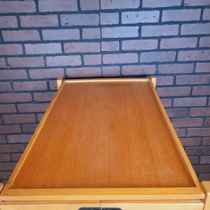 May include: A wooden serving trolley with two shelves and a black metal hinge. The trolley is made of light wood and has a natural finish.