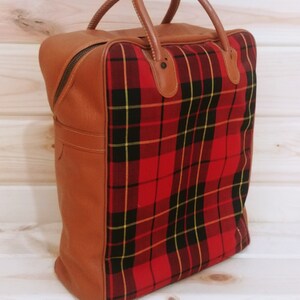 May include: A brown leather travel bag with a red and black plaid lining. The bag has two top handles and a zipper closure.