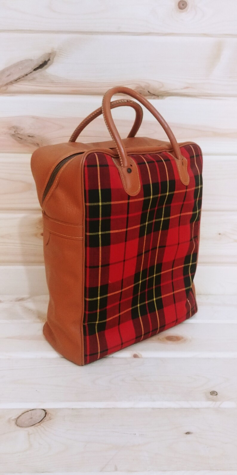 May include: A brown leather travel bag with a red and black plaid lining. The bag has two top handles and a zipper closure.