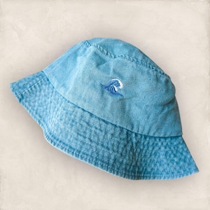 May include: A blue denim bucket hat with a small embroidered wave design.