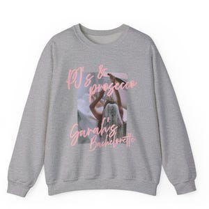 May include: A heather gray sweatshirt with the text "PJ's & Prosecco, Sarah's Bachelorette" in pink script. The graphic in the center shows a person in a bathtub holding a bottle of Prosecco.