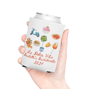 May include: White can cooler with a design of Italian-themed illustrations, including a scooter, a lemon tree, a glass of Aperol Spritz, and a plate of fruit. The text "La Dolce Vita Isabelle's Bachelorette 2024" is printed on the cooler.