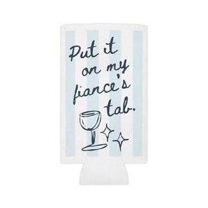 Puede incluir: Enfriador de latas blanco con rayas azules y el texto "Put it on my fiance's tab." Una copa de vino con un brillo se ilustra debajo del texto.