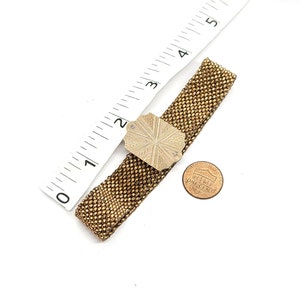 May include: A gold chain bracelet with a decorative silver clasp. The clasp is a square shape with a starburst design.