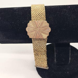 May include: A gold-toned chain bracelet with a decorative, engraved clasp. The bracelet is made of a woven chain pattern.