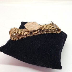 May include: A gold-toned chain bracelet with a decorative, octagonal-shaped clasp. The bracelet is on a black velvet cushion.