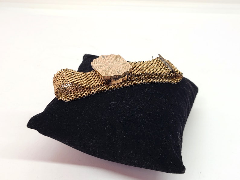 May include: A gold-toned chain bracelet with a decorative, octagonal-shaped clasp. The bracelet is on a black velvet cushion.