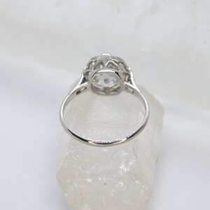 May include: A silver ring with a large, round, clear stone set in a delicate, filigree design.