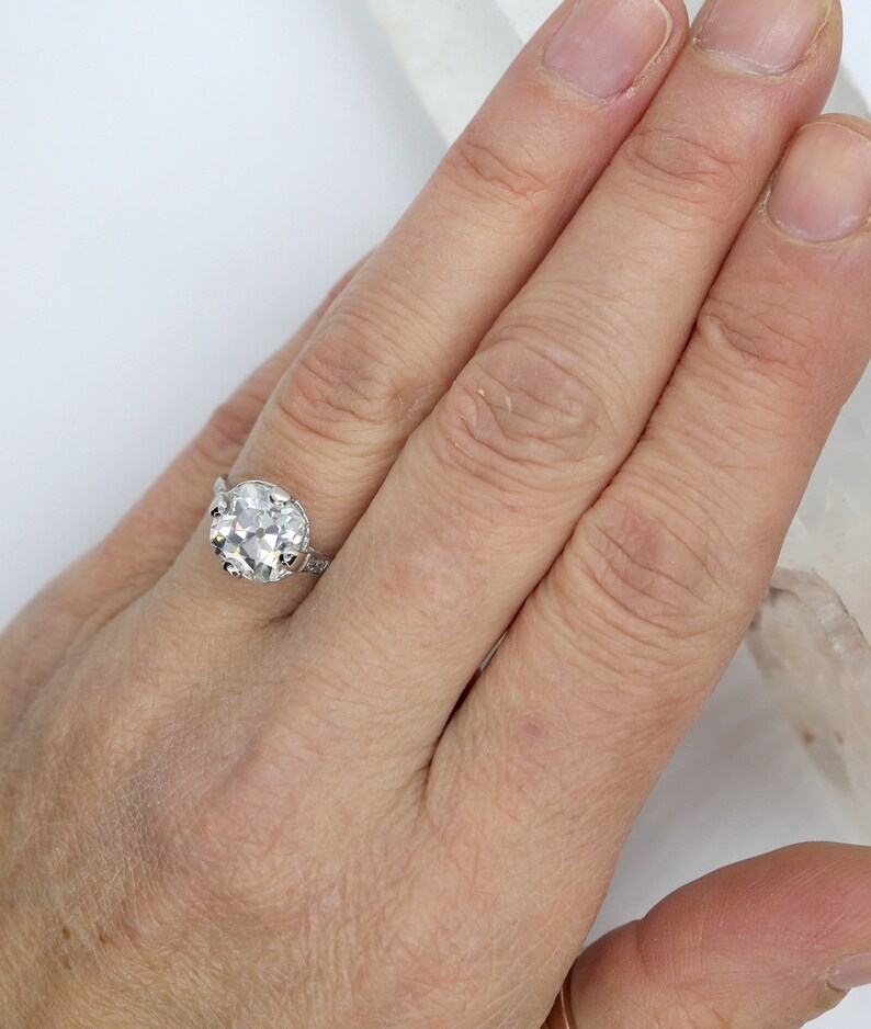 May include: A silver ring with a large, clear, round gemstone set in a claw setting. The ring is on a person's finger.