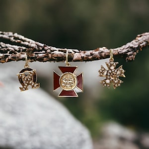 May include: Three gold pendants with pearl accents hanging from a branch. The pendants are a red cross with a gold emblem, a snowflake design, and a Greek letter omega.