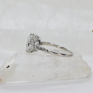 May include: A silver engagement ring with a large, round, clear center stone and smaller stones set in the band.
