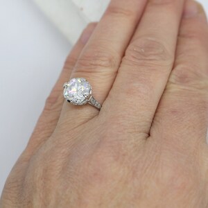 May include: A silver engagement ring with a large, round, clear diamond set in a halo setting. The band is adorned with smaller diamonds.