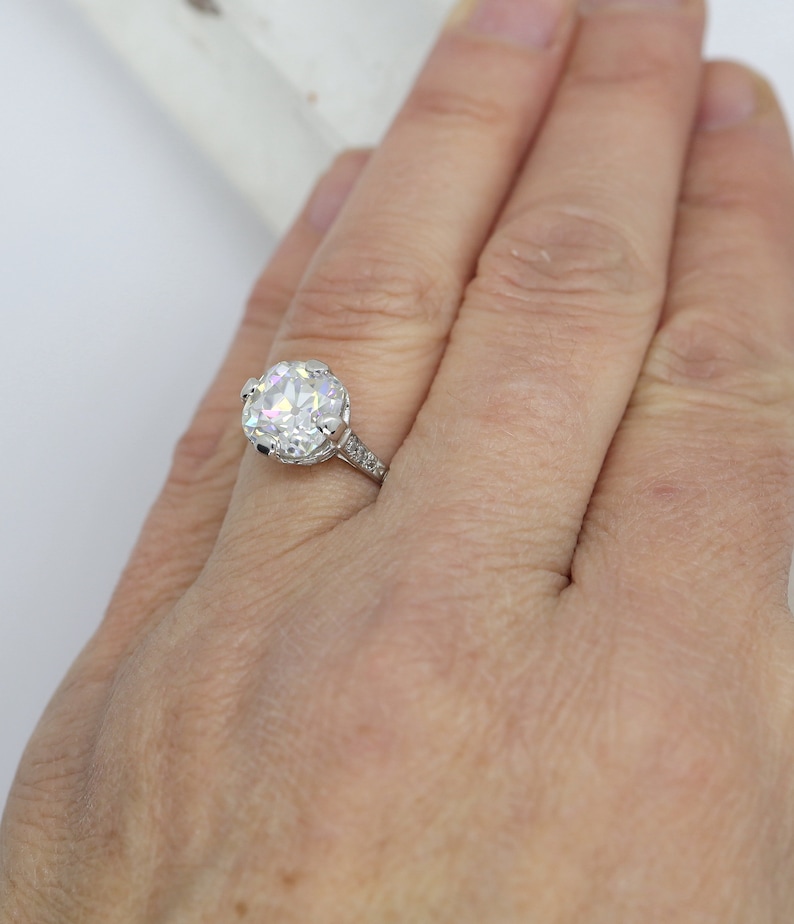 May include: A silver engagement ring with a large, round, clear diamond set in a halo setting. The band is adorned with smaller diamonds.