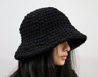 May include: A black crocheted bucket hat with a wide brim. The hat is made of a soft, textured yarn.