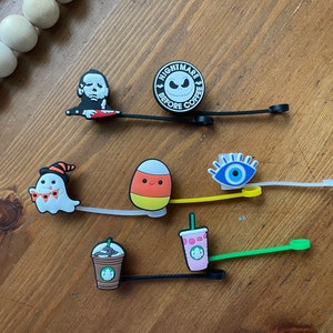 May include: A collection of decorative charms featuring Halloween and coffee-themed designs. Includes a Michael Myers figure, a Jack Skellington design, a ghost, a candy corn, an evil eye, and Starbucks-themed charms.