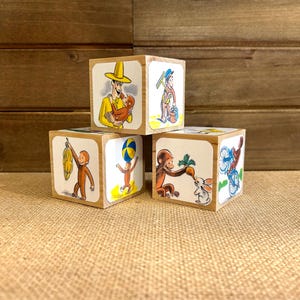 May include: Four wooden blocks with colorful illustrations of a man in a yellow hat holding a monkey, a monkey balancing a ball, a monkey holding a carrot and a rabbit, and a monkey riding a bicycle.