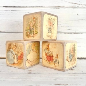 May include: Four wooden blocks with illustrations of Peter Rabbit from the children's book by Beatrix Potter. The blocks feature different scenes from the book, including Peter Rabbit in the garden, Peter Rabbit in the kitchen, Peter Rabbit in the woods, and Peter Rabbit in the meadow.