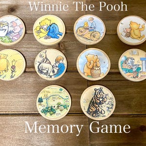 May include: Winnie the Pooh memory game with 10 round wooden tiles featuring different illustrations of Winnie the Pooh and his friends.  The tiles are decorated with images of Pooh Bear, Piglet, Tigger, Eeyore, and other characters from the Winnie the Pooh stories.