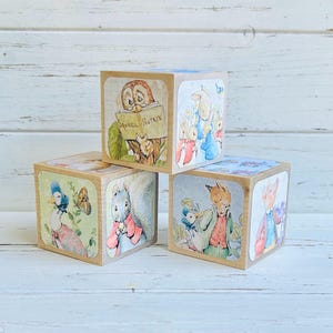 May include: Set of four wooden blocks featuring illustrations from the classic children's book "The Tale of Peter Rabbit". Each block features a different character, including Peter Rabbit, Squirrel Nutkin, Benjamin Bunny, and Jemima Puddle-Duck.