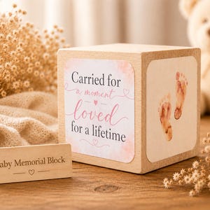 May include: A wooden baby memorial block with the text "Carried for a moment, loved for a lifetime" and baby footprints. A small wooden sign reads "Baby Memorial Block". A teddy bear is in the background.