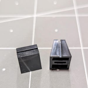 May include: Two black plastic pieces, one is a rectangular block and the other is a triangular prism with a slot in the top.