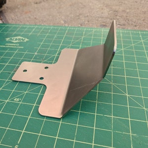 May include: A metal bracket with four holes and a 45-degree angle. The bracket is on a green cutting mat.