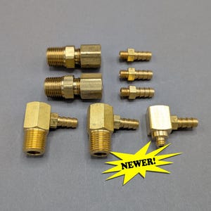 May include: A collection of seven brass hose fittings and adapters, including two straight threaded connectors, three small barbed hose connectors, and two elbow-shaped barbed fittings, with a yellow starburst graphic containing the text NEWER!