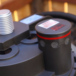 May include: Close-up of a black pump with a red and black safety cap. The cap has a warning label that reads "DANGER HIGH VOLTAGE. ELECTRIC SHOCK HAZARD. REMOVE POWER BEFORE SERVICING OR ADJUSTMENT."