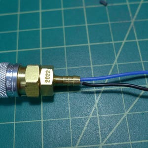 May include: A brass air fitting with a silver threaded connector and a blue and black wire attached. The fitting is labeled "2022".