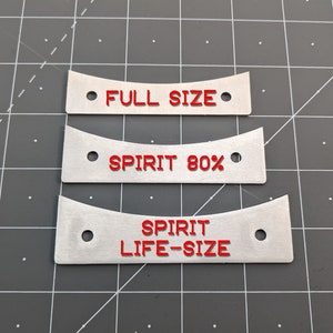 May include: Three brushed metal tags with red lettering. The top tag reads "FULL SIZE", the middle tag reads "SPIRIT 80%", and the bottom tag reads "SPIRIT LIFE-SIZE". Each tag has two holes and a curved design.