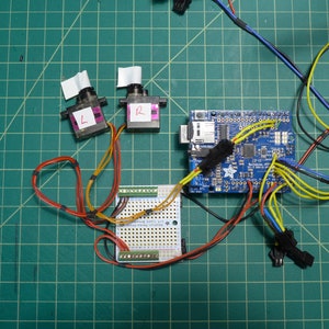 May include: A blue circuit board with wires connected to two small black motors labeled "L" and "R". The motors are connected to a breadboard with a yellow and orange wire.