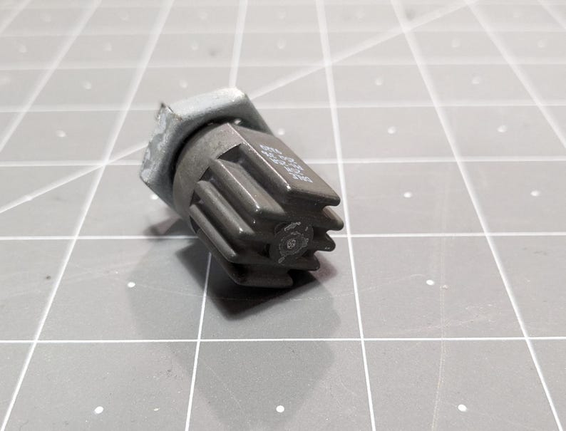 May include: A gray metal electrical component with a hexagonal shape and a series of ridges on the side. The component has a small hole in the center.