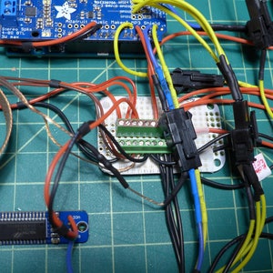 May include: A close-up of a circuit board with various wires and connectors. The wires are color-coded, including red, black, blue, yellow, and green. The circuit board has a green terminal strip with multiple pins. The wires are connected to the terminal strip and other components on the board.