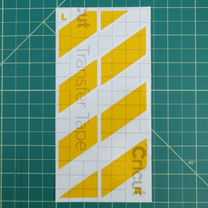 May include: Yellow diagonal stripes on a white background with the text "Cricut Transfer Tape" on the left side and "Cricut" on the right side.