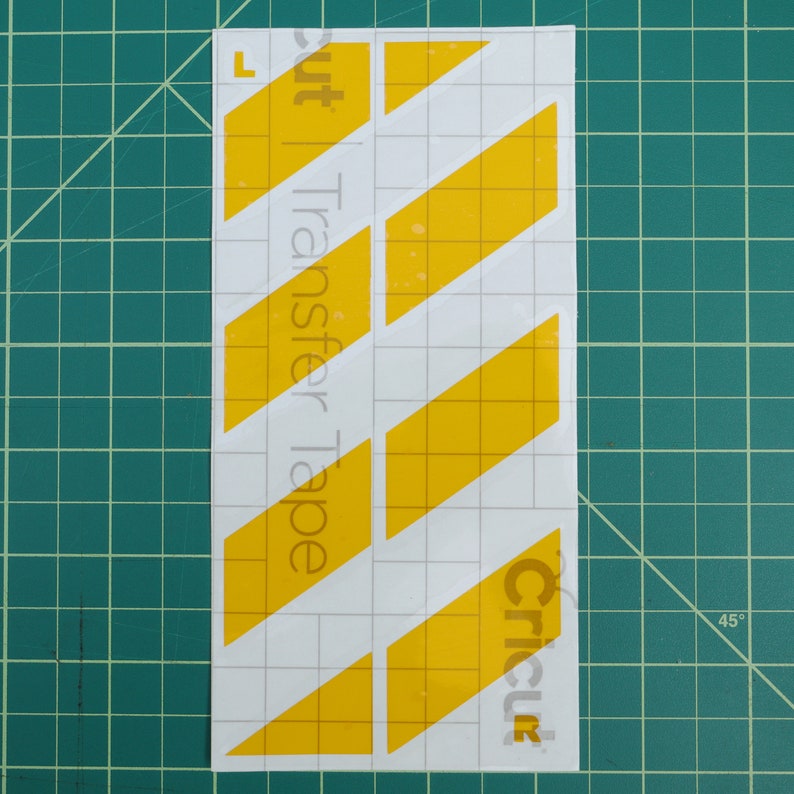 May include: Yellow diagonal stripes on a white background with the text "Cricut Transfer Tape" on the left side and "Cricut" on the right side.