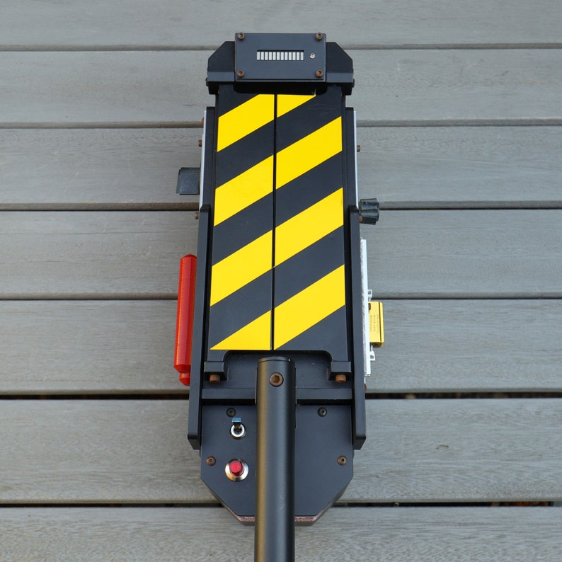 May include: Black and yellow striped ghost trap prop with a red button and a black handle. The trap has a digital display with the text "0000".