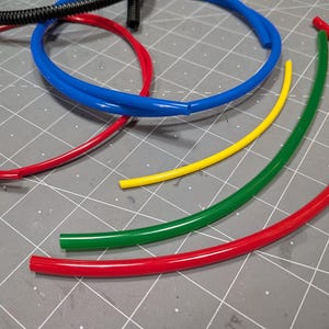 May include: A collection of flexible plastic tubing in various colours including red, blue, yellow, and green. The set includes two red circular loops, one blue circular loop, one yellow curved segment, and one green curved segment of tubing.