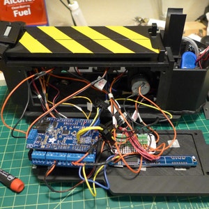 May include: A close-up of a black and yellow striped box with wires and a blue circuit board inside. The box is open and the circuit board is visible. There are also some other electronic components inside the box.