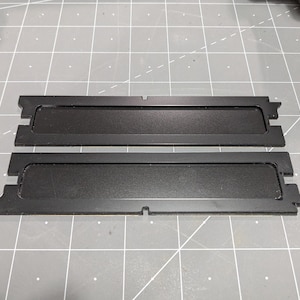 May include: Two black plastic RAM memory modules. The modules are rectangular and have a black plastic cover with a silver trim.