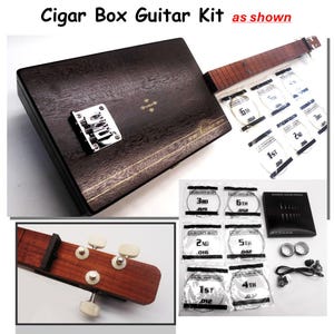 May include: A cigar box guitar kit with a dark brown wooden box, a fretboard, and a variety of guitar strings. The kit includes a bridge, tuning pegs, and other components for assembly. The text "Cigar Box Guitar Kit as shown" is visible.